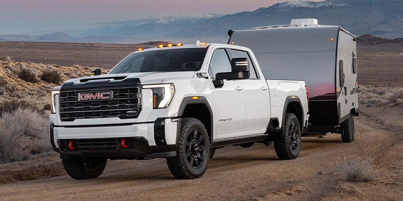 Photograph of a white 2025 GMC Sierra 2500HD towing a trailer