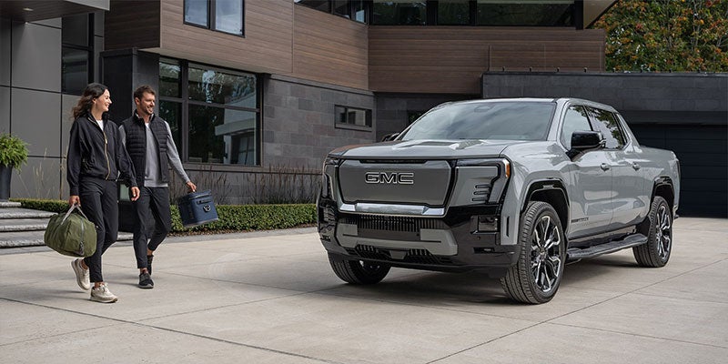 Photograph of a 2025 GMC Sierra EV Denali staged in front of a house with a couple walking next to it